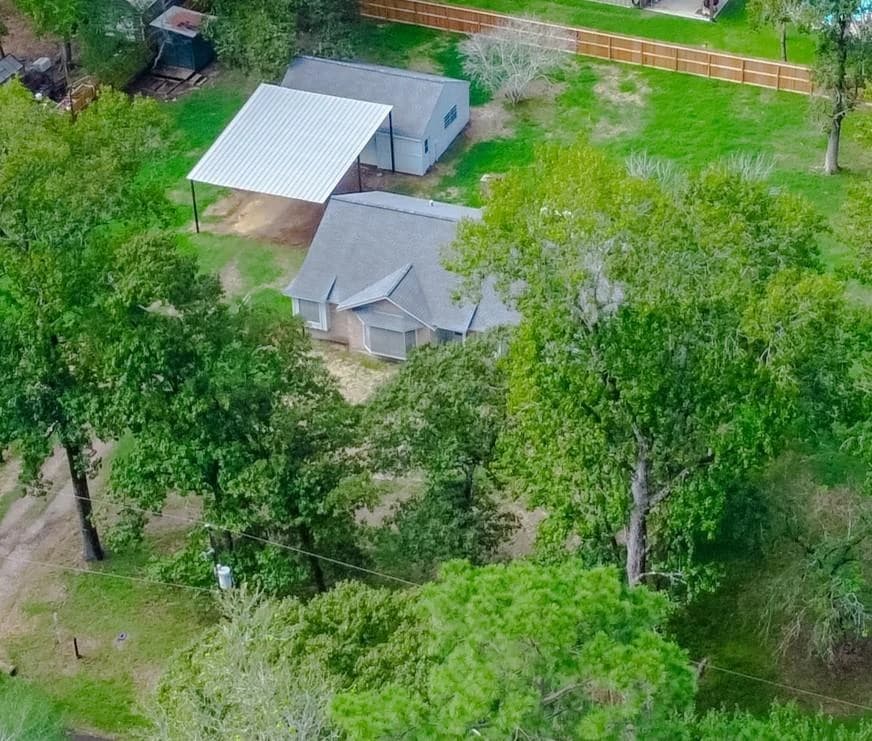 Aerial view of a one story home with a detached garage and a metal RV carport on a wooded lot in Stagecoach Farms, Stagecoach, Texas